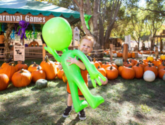 Child holding a green balloon among pumpkins at Irvine Park Railroad