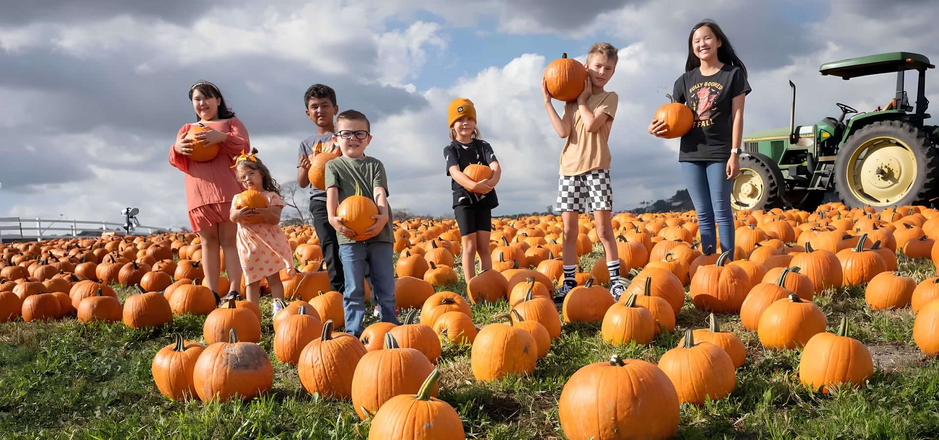 Children standing in a pumpkin patch beside a tractor at Kellogg Ranch
